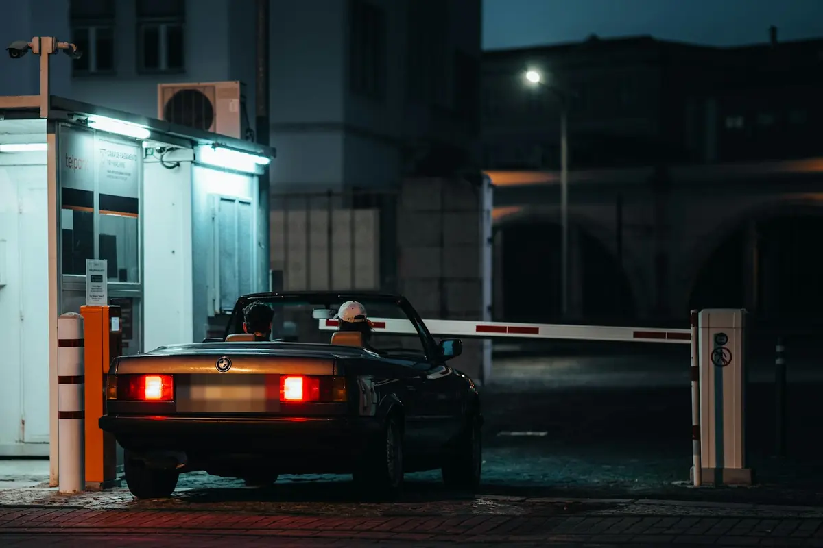 Noční záběr na vjezd do areálu: auto stojí u závory vedle vrátnice a je označené rámečkem